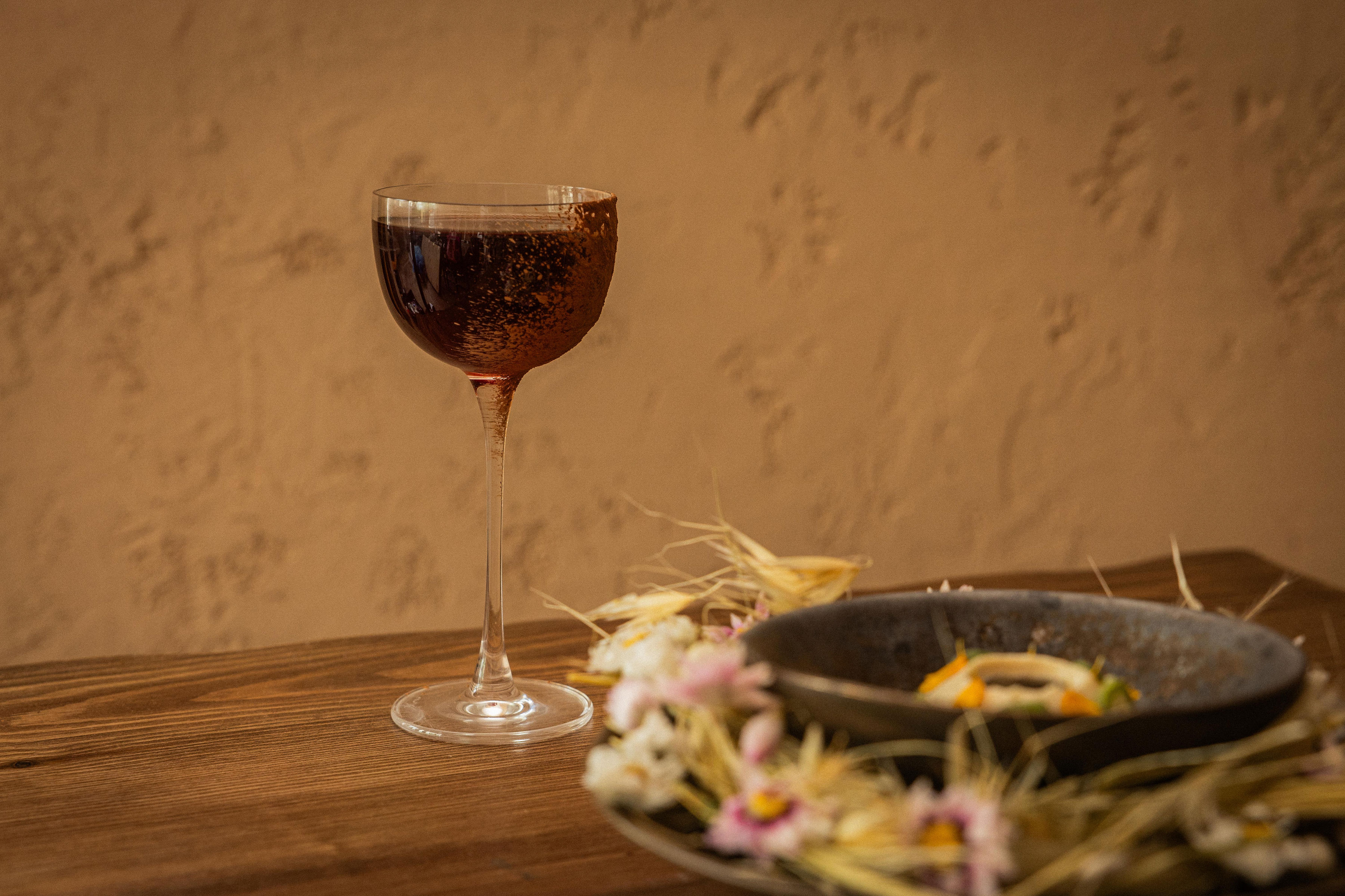 Glass of red wine and a bowl of food garnished with flowers and straw.